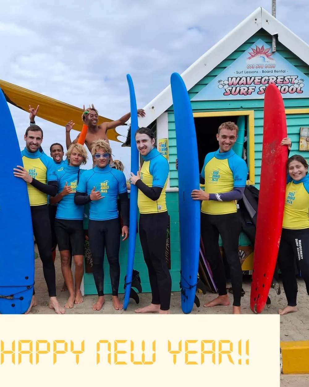 A group of surf students holding their boards outside the Wavecrest Surf School shop on Dolphin Beach