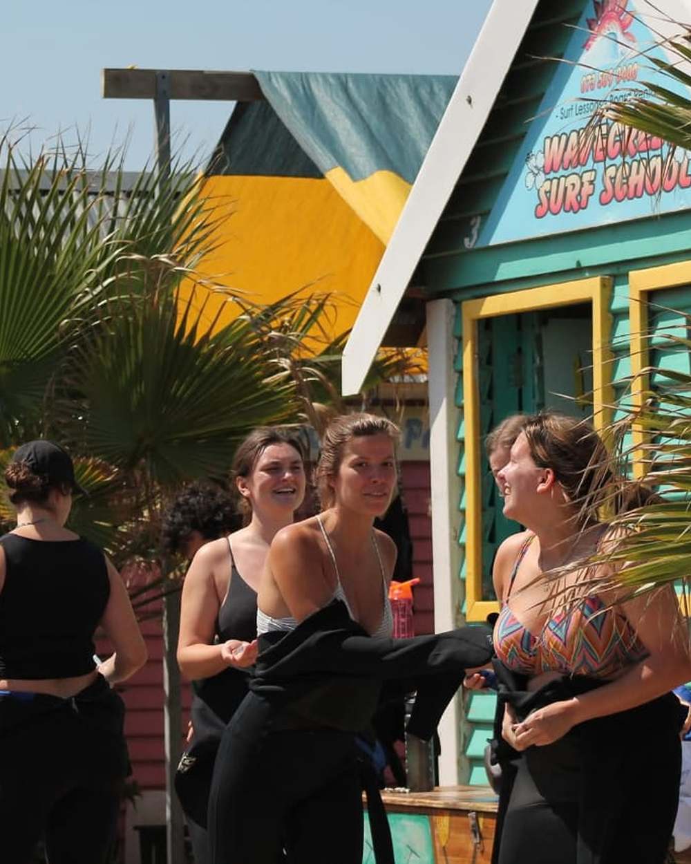 Surf students pulling on wetsuits outside the Wavecrest Surf School shop before a lesson in Jeffreys Bay